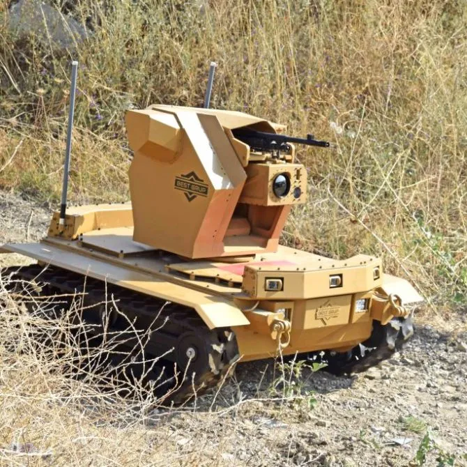 Sarı-kahverengi FEDAİ paletli robotunun, üzerinde makineli tüfek bulunan silah kulesiyle otların arasında görünümü, gövdesinde Best Grup logosu