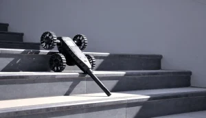 Elektroland ACROB keşif robotu, siyah dört tekerlekli kompakt gövde, merdiven basamağına yaslanmış uzun anten/kol