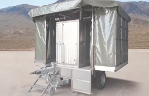 Çadır örtülü, merdivenli bir banyo-tuvalet treyleri, dağlık arazi arka planında