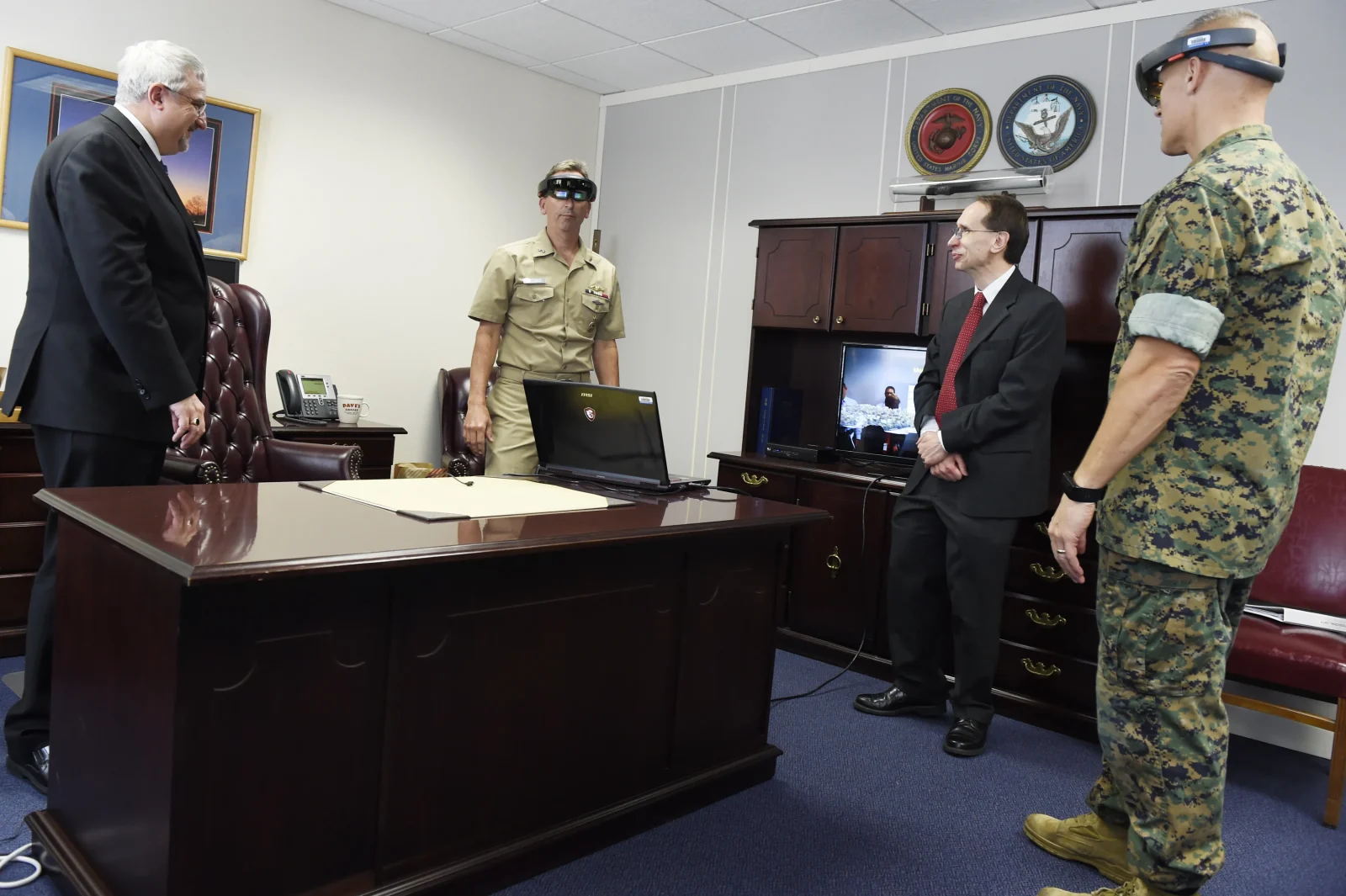 En una sala de instrucción, personal militar prueba un dispositivo de visualización montado en la cabeza mientras asistentes civiles observan