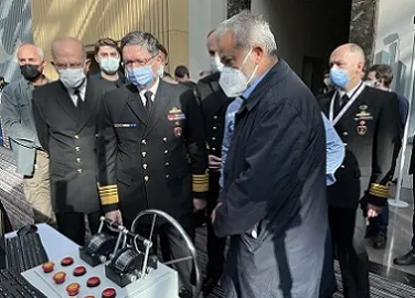 ضباط بحريون بالزي الرسمي ومشاركون يقفون أمام منصة تحكّم لمحاكٍ مزوّدة بدفة قيادة