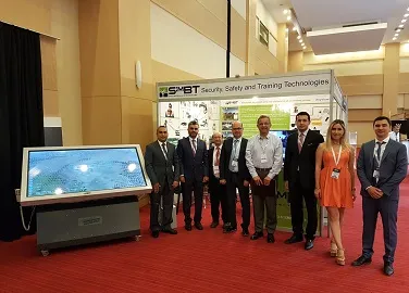 Qué es HoloTable: el cajón de arena holográfico de SimBT 4 El equipo de SimBT junto a una mesa táctil horizontal que muestra un mapa, en un estand de feria