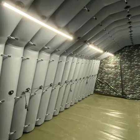 Şi̇şi̇ri̇lebi̇li̇r Airbeam Çadirlar 8 Bir şişirilebilir çadırın iç kısmında toplantı düzeninde dizilmiş masalar ve sandalyeler, arka planda kamuflaj desenli bir perde/kapı bölümü, tavanın kemerli hava kirişi yapısı